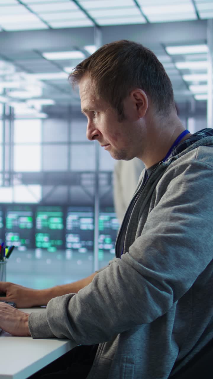 Vertikal video: Portrett av smilende ingeniør som inspiserer serverrader i et datasenter.