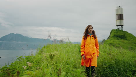 woman in orange raincoat hiking on a coastline