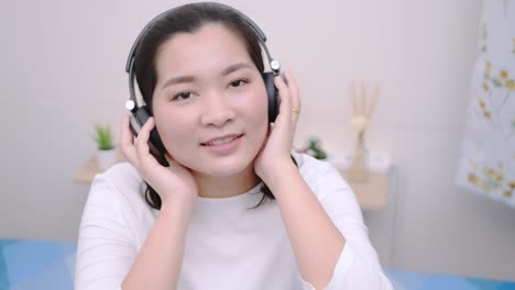 asian woman smiling using the bluetooth headphone for listening to music and looking at the camera so lovely lie in bed