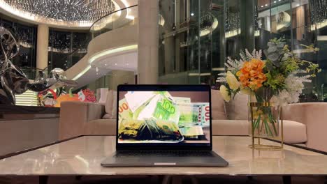 Laptop-Displaying-Falling-100-Dollar-Bills-Money-Inside-Luxury-Mansion-Interior