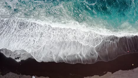 olas cristalinas del océano turquesa que lavan la playa de arena negra, arriba