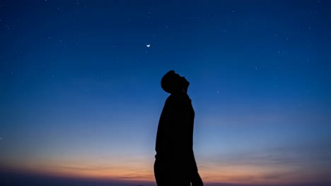 silhouette of a person gazing at the starry night sky with a crescent moon