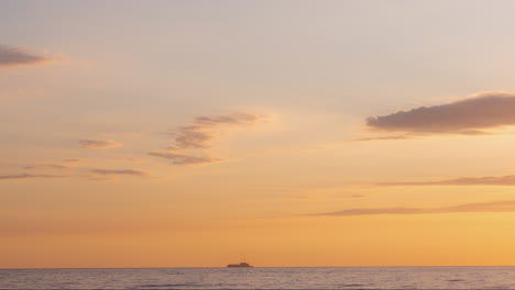 Cargo-ship-moving-across-an-orange-ocean-sunset-time-lapse-small-clouds