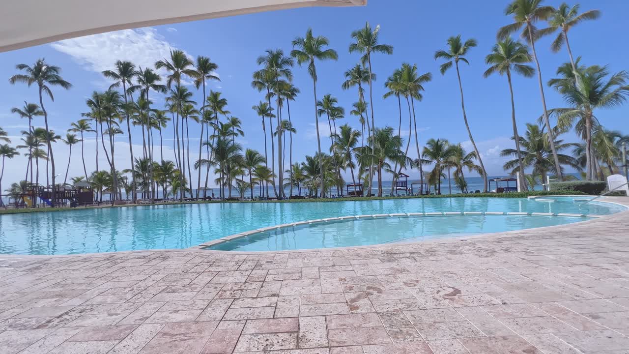 En smuk swimmingpool på et caribisk hotel, omgivet af palmer mod en blå himmel