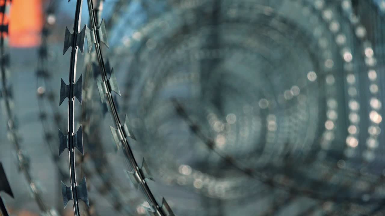 Close-up of spiral razor wire on a high-security fence, with metallic glints and a layered depth, symbolizing restriction and protection.