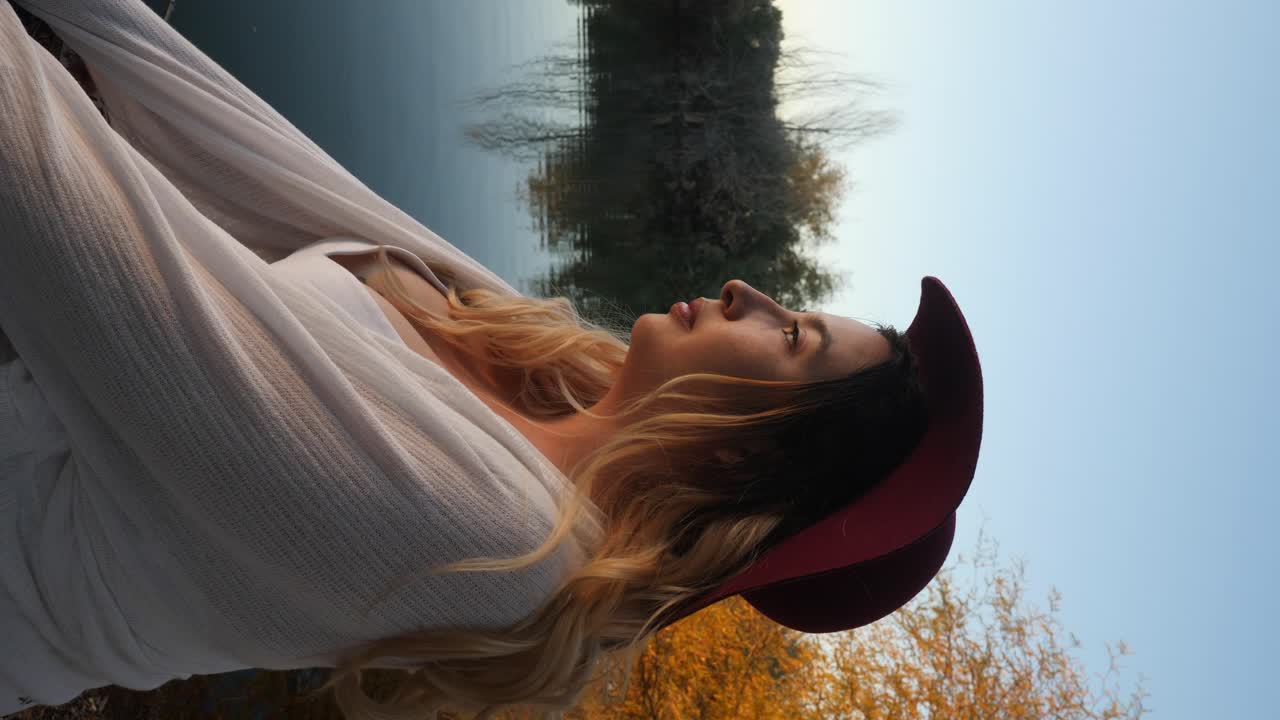 Fashionable woman in white flips her hair next to calm water