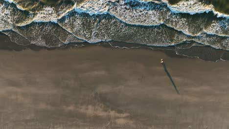 beautiful cinematic drone shot of couple walking on the beach during sunset