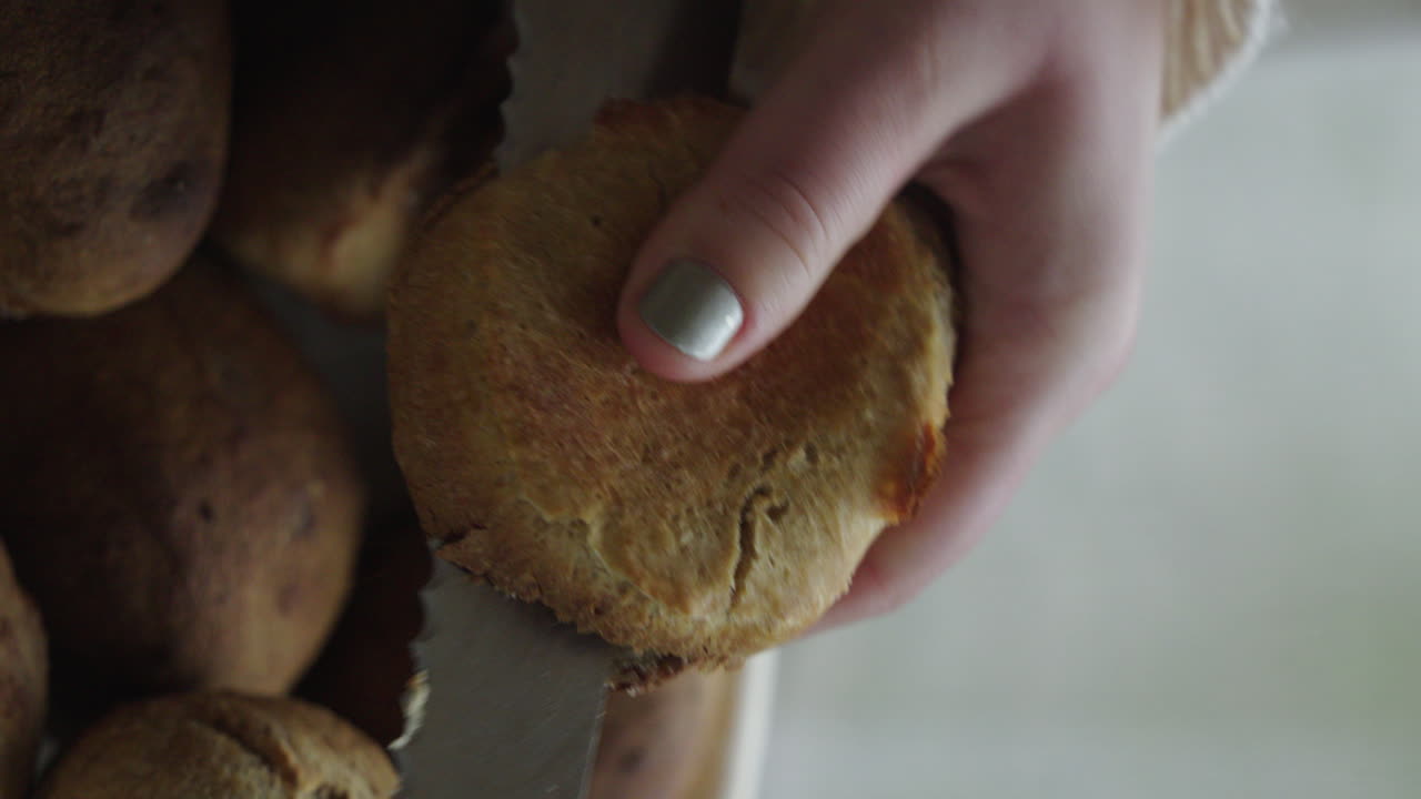manos de una mujer cortando un bollo de pan casero fresco o un bollo de pan con un cuchillo afilado pan europeo vertical de cerca