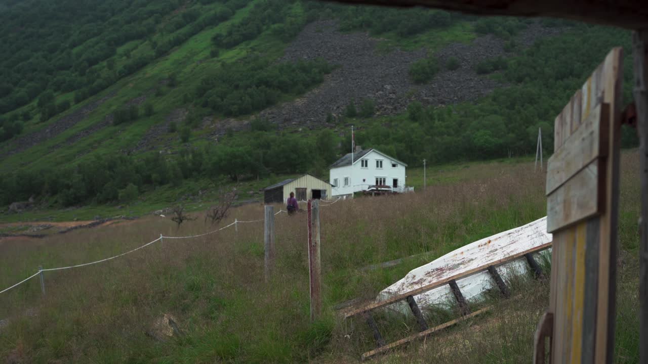 mujer caminando por un camino cubierto de hierba con su perro mascota a la casa al pie de la montaña en flakstadvag, noruega