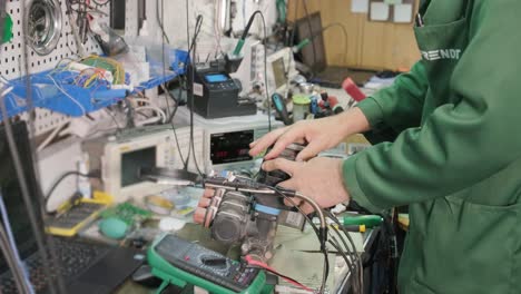 electronic equipment repair shop. the engineer technician solders the printed circuit board of an electronic device under a microscope.