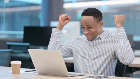 successful african businessman celebrating on laptop at work