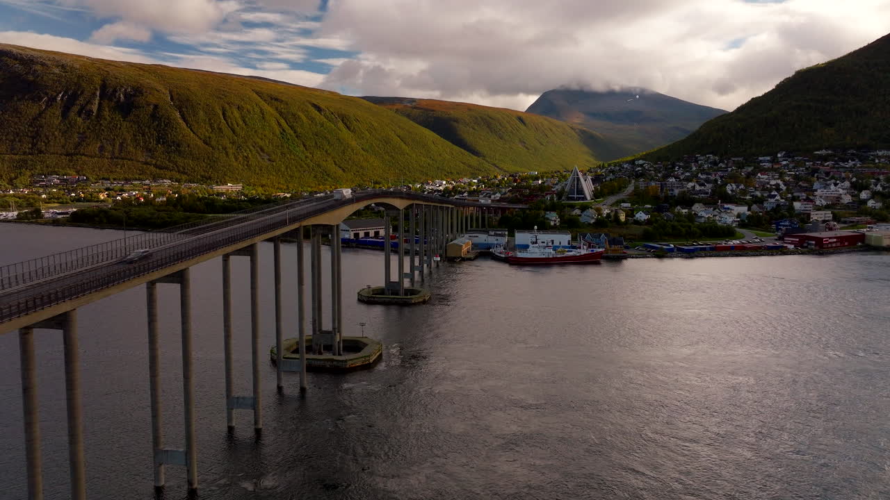 Drönarvy över Tromsø bro med trafik, ikoniska Ishavskatedralen med höstfärgade berg i bakgrunden, Norge