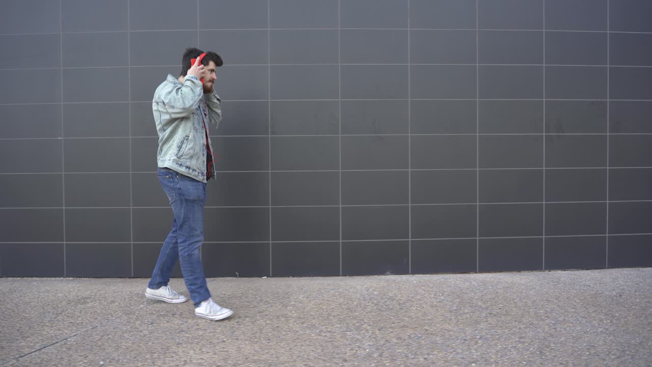 l'uomo indossa le cuffie rosse e cammina guardando il cellulare rosso