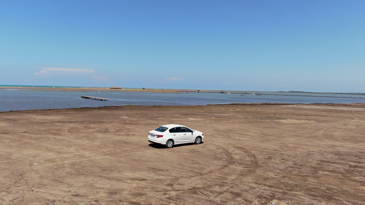 coche blanco conduciendo a lo largo de la orilla de la laguna karavasta en albania y en un día soleado