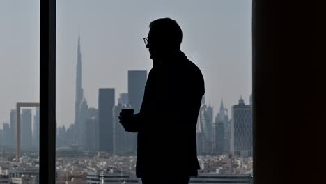 4k: silhouette of a businessman talking over the phone by the window, the world's tallest building 'burj khalifa' in the background