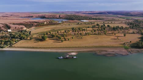 Aerial-wide-shot-of-a-dredger-unloading-dredged-sand-on-a-big-river,-sunny-day