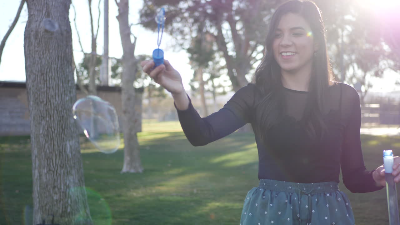 Attractive young woman blowing bubbles and smiling with joy and happiness as she has fun playing in the sunlight