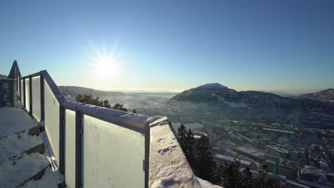 motion shot along frozen railings with sunflare, bergen city views as background