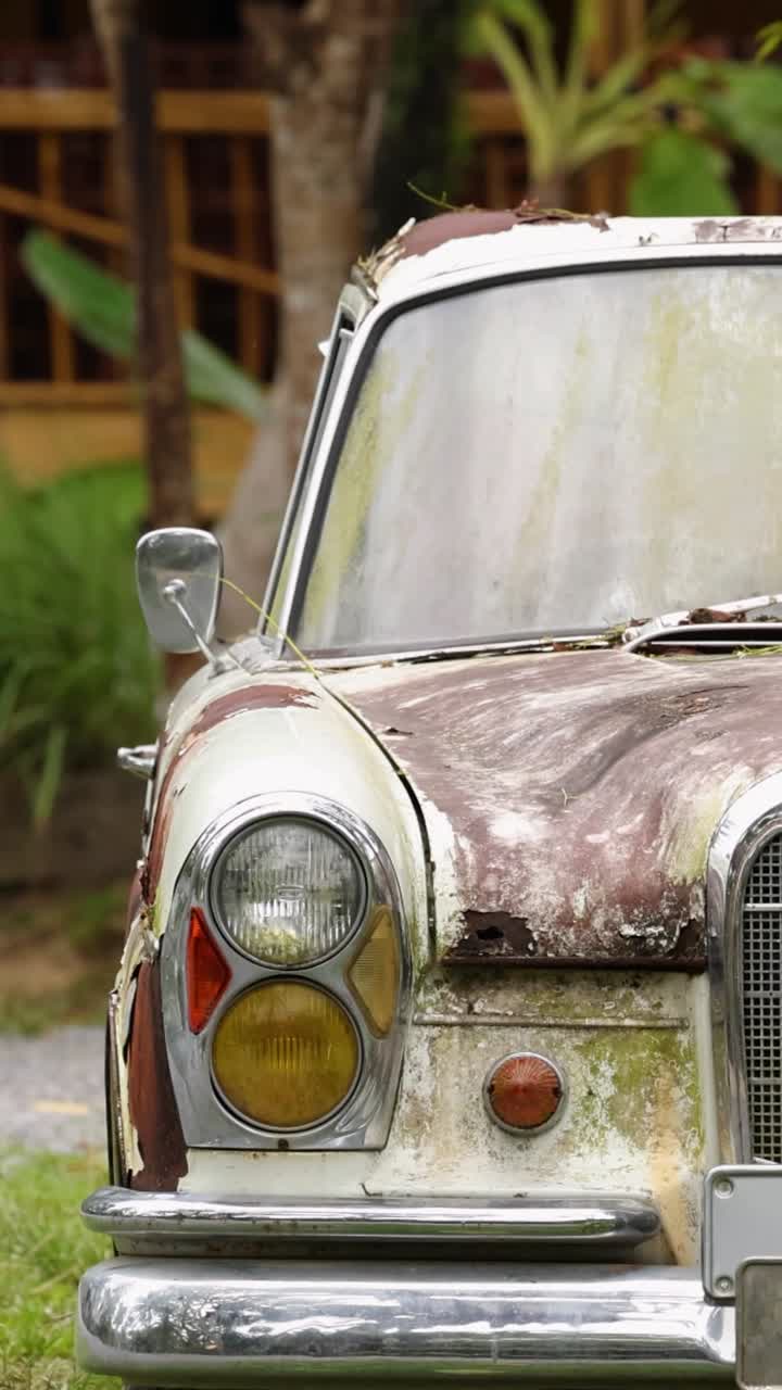 A weathered vintage car sits amidst lush greenery in a tranquil garden setting, captured with natural lighting in Phuket, Thailand