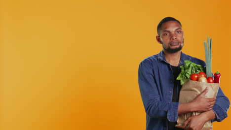 retrato de un hombre afroamericano sosteniendo una bolsa de papel llena de comida biológica