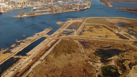 Drone-shot-of-a-shore,-river-and-flooded,-excavated-area-with-port-in-the-distance