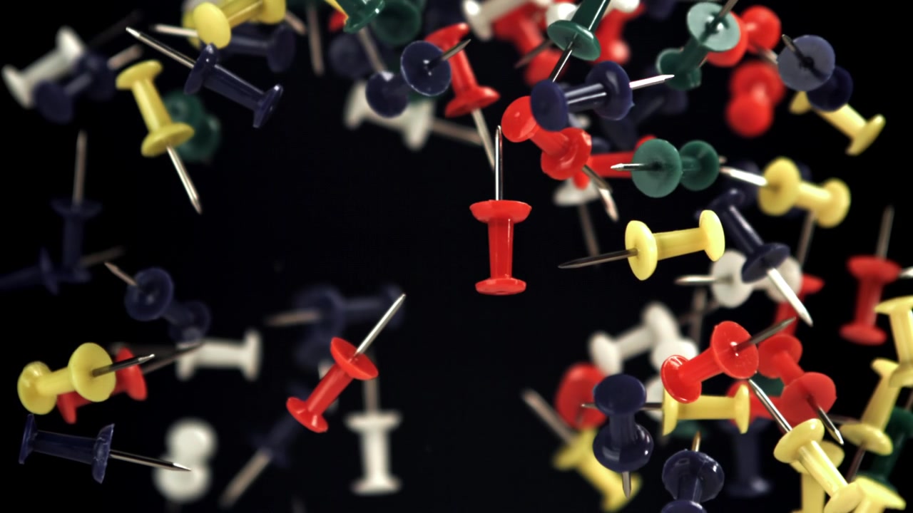 Colorful Pushpins Floating and Falling Against a Black Background