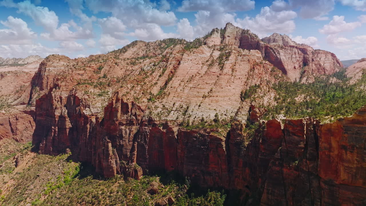 Flying closer to the rugged rock in Zion National Park. Beautiful canyons of America at the backdrop of blue sky with clouds.