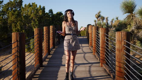 una hermosa joven escuchando música desde su teléfono inteligente con sus auriculares mientras camina por un puente en cámara lenta de la naturaleza