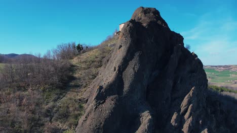 Aerial-footage-of-Pietra-Perduca,-volcanic-rock,-church-set-at-top-stone-immersed-in-countryside-landscape,-cultivated-land-in-Val-Trebbia-Bobbio,-Emilia-Romagna,-Italy