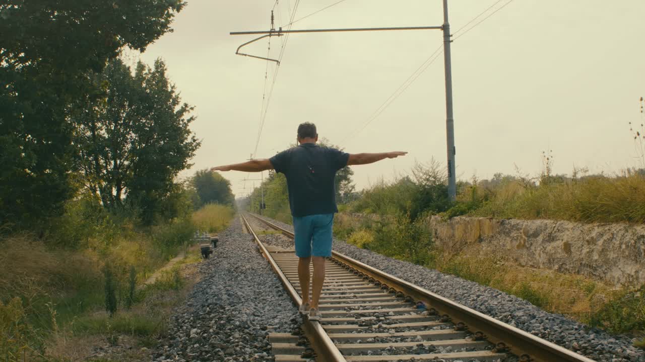 A man plays tightrope walker on the tracks of a train at a possibly abandoned station