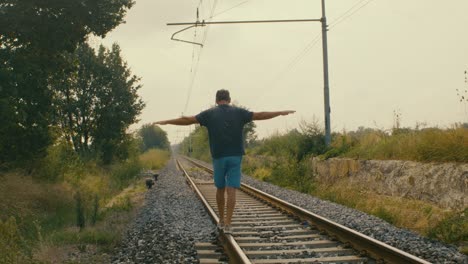 a man plays tightrope walker on the tracks of a train at a possibly abandoned station