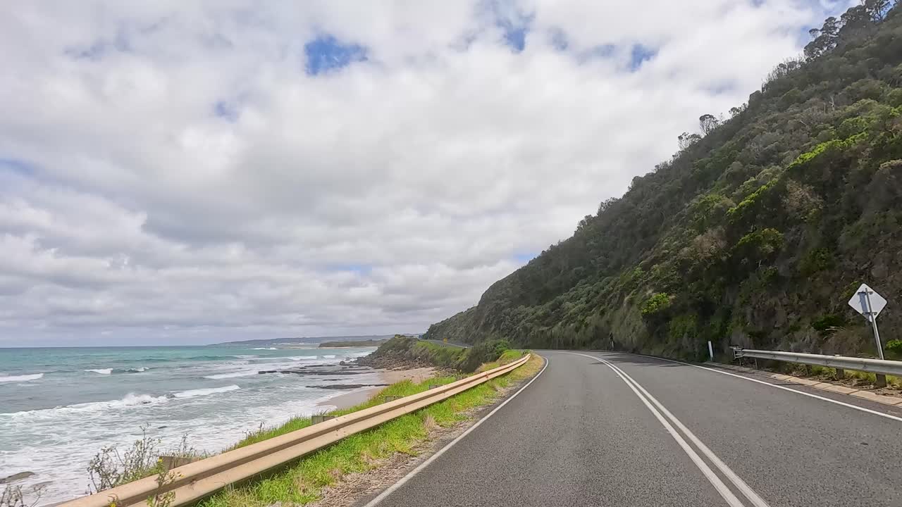 A 15-second video captures a coastal drive on Great Ocean Road, showcasing ocean views, winding roads, and lush greenery under a cloudy sky