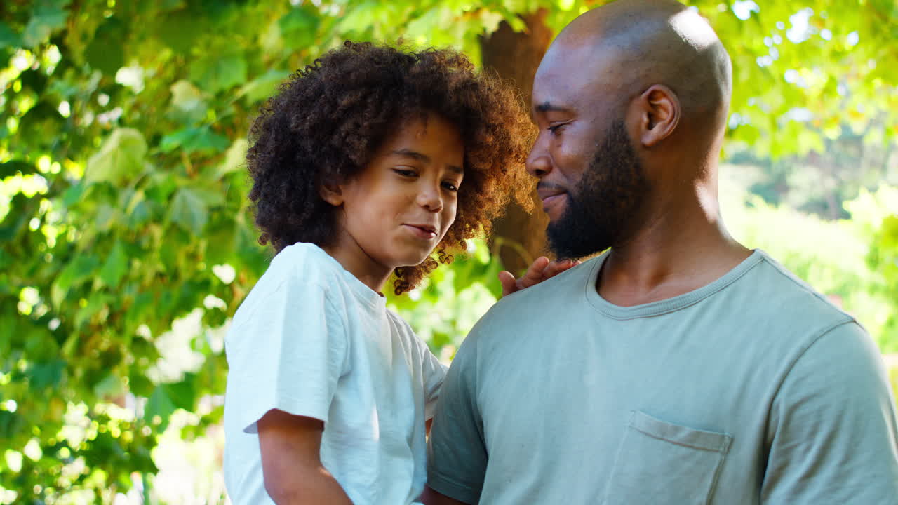 Padre amorevole che tiene in braccio il figlio in un giardino estivo con alberi