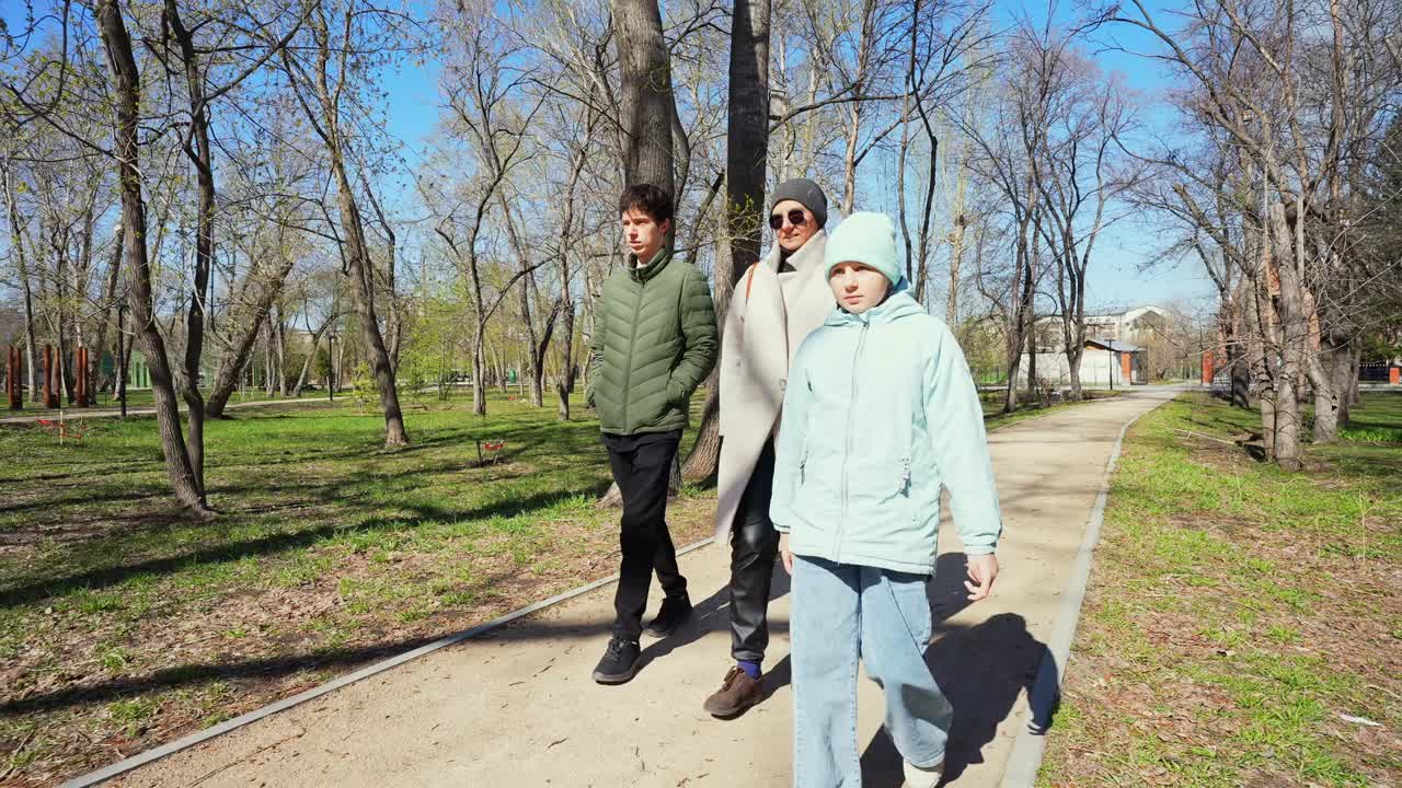 Tre personer går sammen på en sti i en solrik park