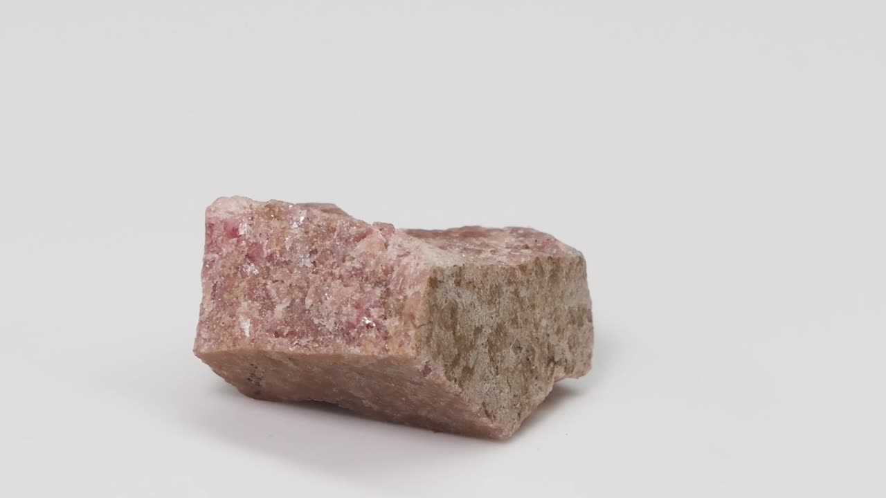 A detailed pink epidosite rock specimen rotates slowly against a clean white studio background