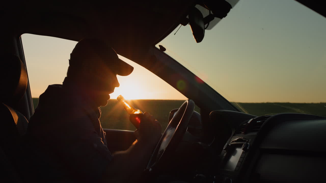 Silhouette of a man who drinks beer while driving a car