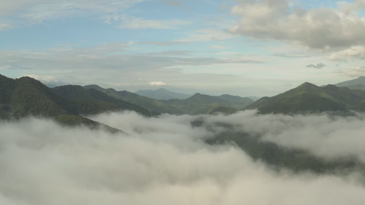 Flying through the clouds above green mountain tops. Aerial view of foggy rainforest