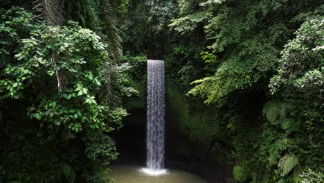 high aerial dolly of tranquil pool and cascading tibumana waterfall amidst tropical jungle with lush green vegetation