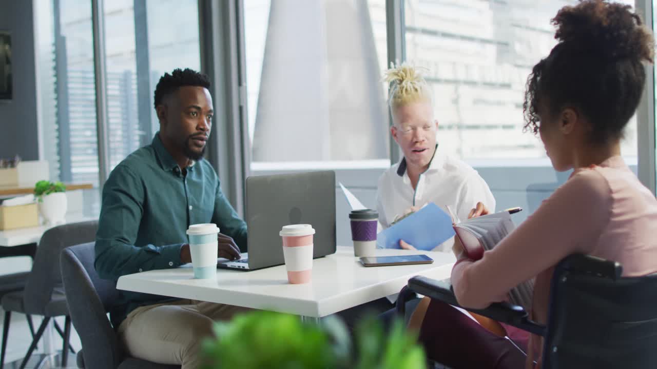 Diverse business people discussing with disabled colleague and documents in creative office