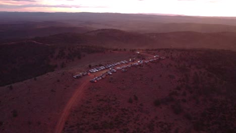 Drone-shot-looking-down-on-many-cars-parked-on-the-top-of-a-hill-with-a-beautiful-sunset-in-the-background