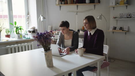 Two-woman-friends-spend-leisure-and-using-notebook-sitting-at-table