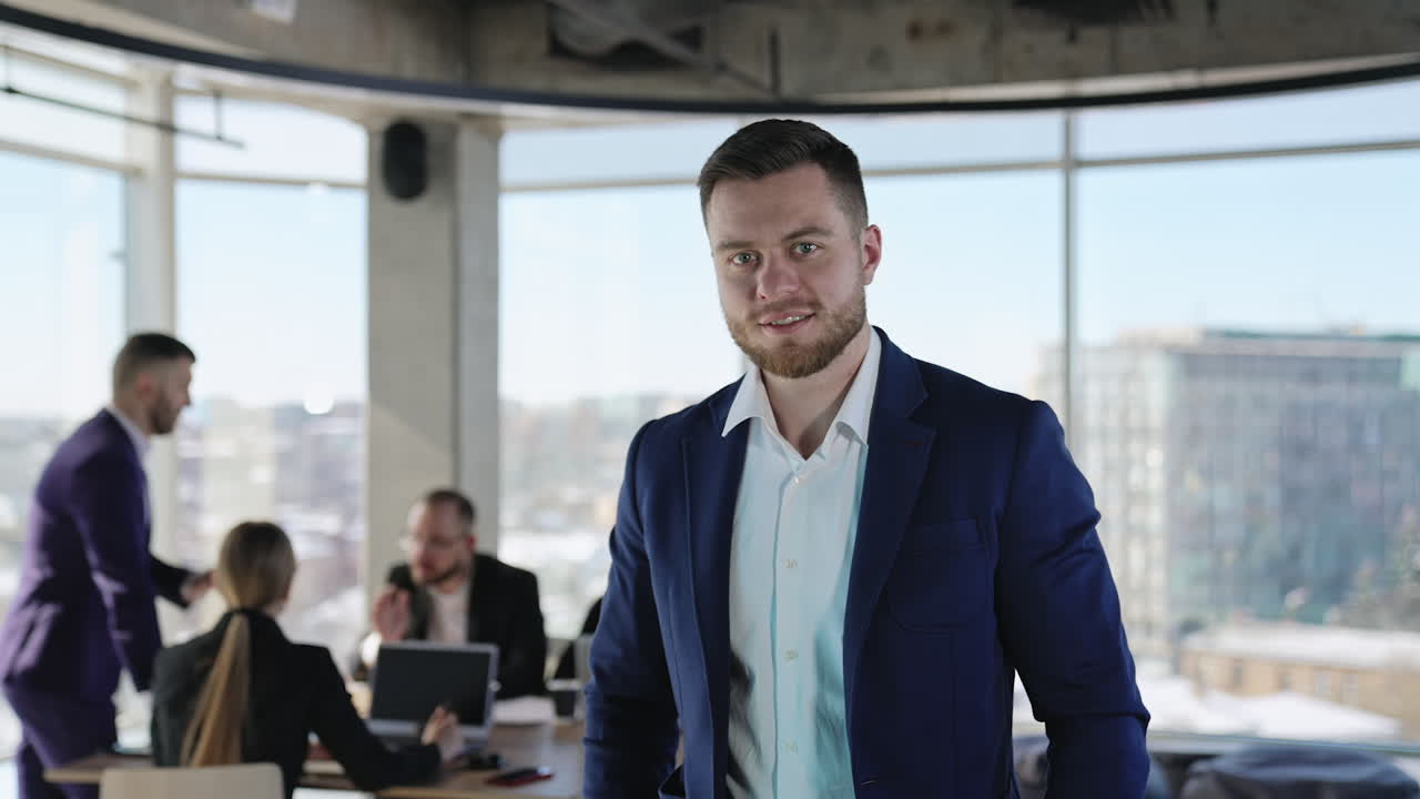 Handsome adult young businessman in dark blue jacket looking straight at camera. Portrait of a modern business owner. Team communicating at backdrop.