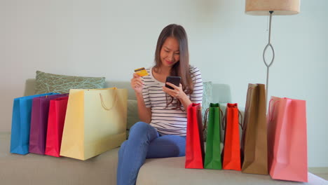 young woman using her credit card or debit card and her mobile phone while shopping online in the comfort of her own home