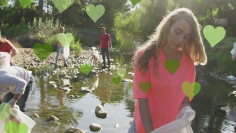 animation of green hearts over diverse happy group picking up rubbish in countryside