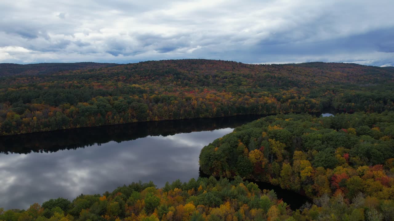 la belleza impresionante de un bosque de otoño, con árboles de color naranja y rojo vibrantes, nubes llenas de lluvia y el tranquilo embalse que refleja el cielo como un espejo