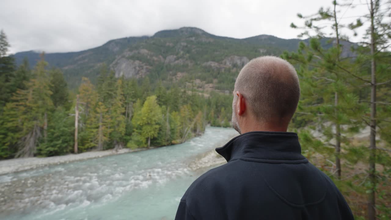 Wide shot of man looking out over river and woodland from ridge lookout