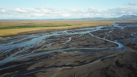 aerial view capturing a glacial river winding through icelandic plains, forming intricate patterns of water and sediment against a backdrop of mountains and clouds, near seljalandsfoss waterfall