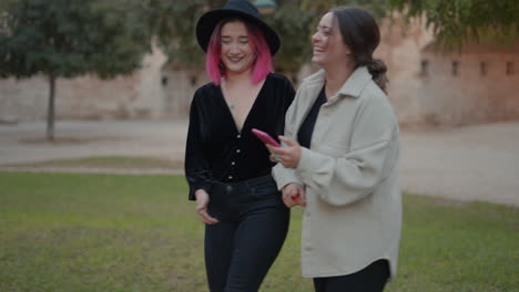 two women walking and looking at a phone in a park