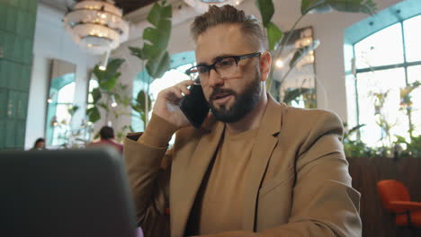 Hombre-De-Negocios-Hablando-Por-Teléfono-Y-Trabajando-En-Una-Laptop-En-Un-Restaurante