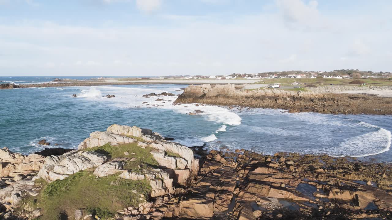 Volo sopra onde spumeggianti che si infrangono a riva su spiaggia e rocce in una giornata di sole splendente a Guernsey, Isole del Canale